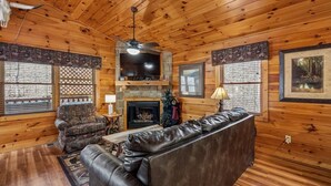 L’intérieur d’un chalet en bois, avec une cheminée, un canapé en cuir et un téléviseur.
