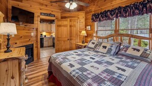 Une chambre de style rustique avec un lit, un ventilateur de plafond, une cheminée, une télévision et un coin cuisine.