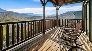 A wooden deck with a railing, a covered area, and a view of mountains.