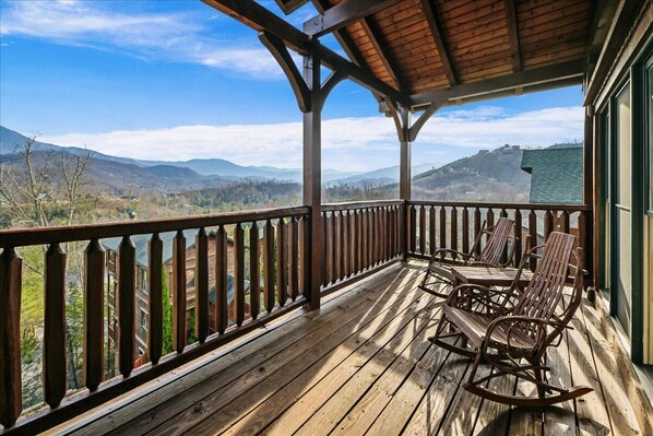 A wooden deck with a railing, a covered area, and a view of mountains.
