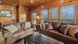 A wooden cabin interior with two leather sofas, a wooden coffee table, and a dining table.