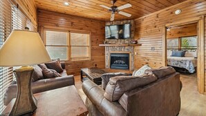 A log cabin interior with a fireplace, leather furniture, and a ceiling fan.