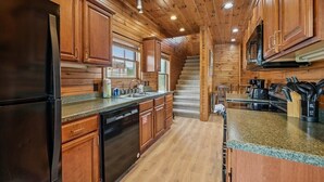 A log cabin-style kitchen with wooden cabinets, a black refrigerator, granite countertops, and a built-in oven.
