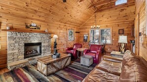 A log cabin interior with a stone fireplace, leather furniture, and a ceiling fan.