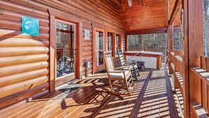 A log cabin with a porch, rocking chairs, a table, and a sign welcoming guests to the cabin.