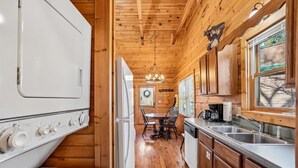 A compact kitchen with wooden walls, a dining area with a table and chairs, and a large appliance on the left.