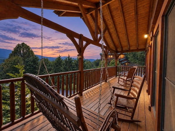 A wooden deck with a swing chair and a rocking chair, overlooking a forested landscape.
