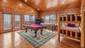 A wooden cabin interior with a pool table, a foosball table, and a bunk bed.