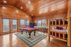 A wooden cabin interior with a pool table, a foosball table, and a bunk bed.