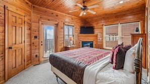 A wooden cabin bedroom with a bed, a ceiling fan, a fireplace, and a TV.