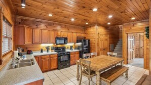 A wooden cabin-style kitchen with a dining table and chairs, built-in appliances, and a staircase leading to another level.