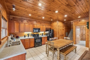 A wooden cabin-style kitchen with a dining table and chairs, built-in appliances, and a staircase leading to another level.
