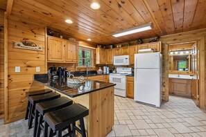 Een houten keuken in cottage-stijl met een centraal eiland, barstoelen, een koelkast en een magnetron.