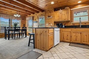A wooden cabin interior with a kitchen area, dining table, and chairs. - Smoky Mountain Log Cabin w/ Hot Tub (Pigeon Forge)