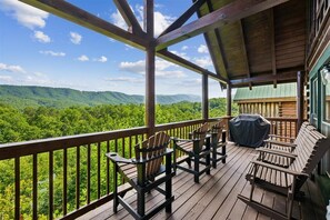 A wooden deck with Adirondack chairs and a barbecue grill, overlooking a forested landscape. - Smoky Mountain Log Cabin w/ Hot Tub (Pigeon Forge)