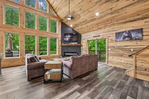 A spacious living room with a fireplace, large windows, and a cozy seating area. - Stylish Modern Mountain Haven w/ Hot Tub (Gatlinburg)