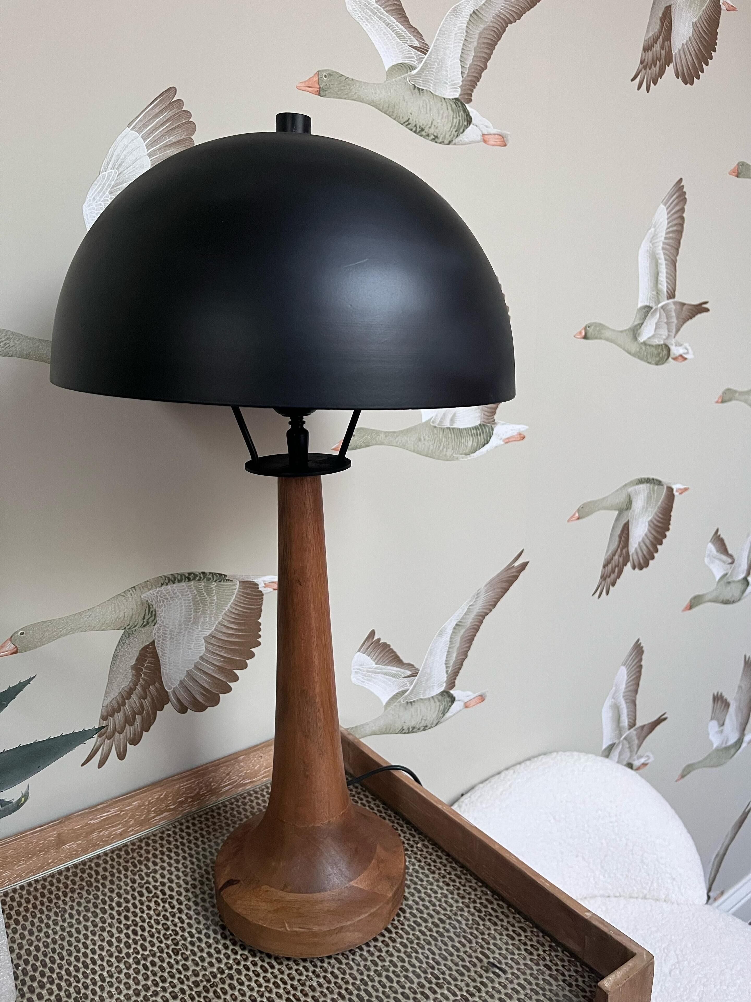 A lamp with a wooden base and a black shade, placed on a textured surface.