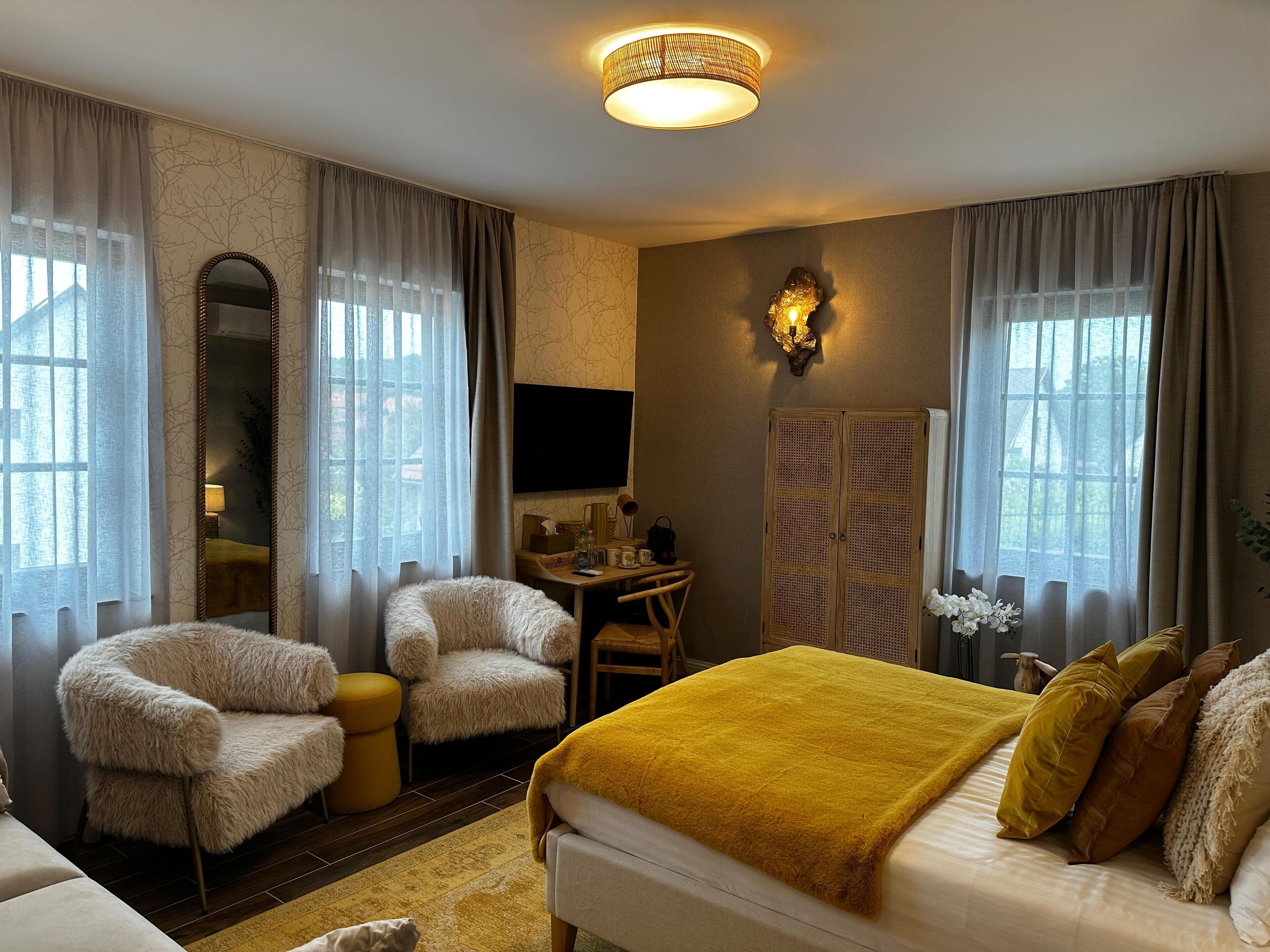 A hotel room with a bed, two armchairs, a desk, a television, and a wardrobe.