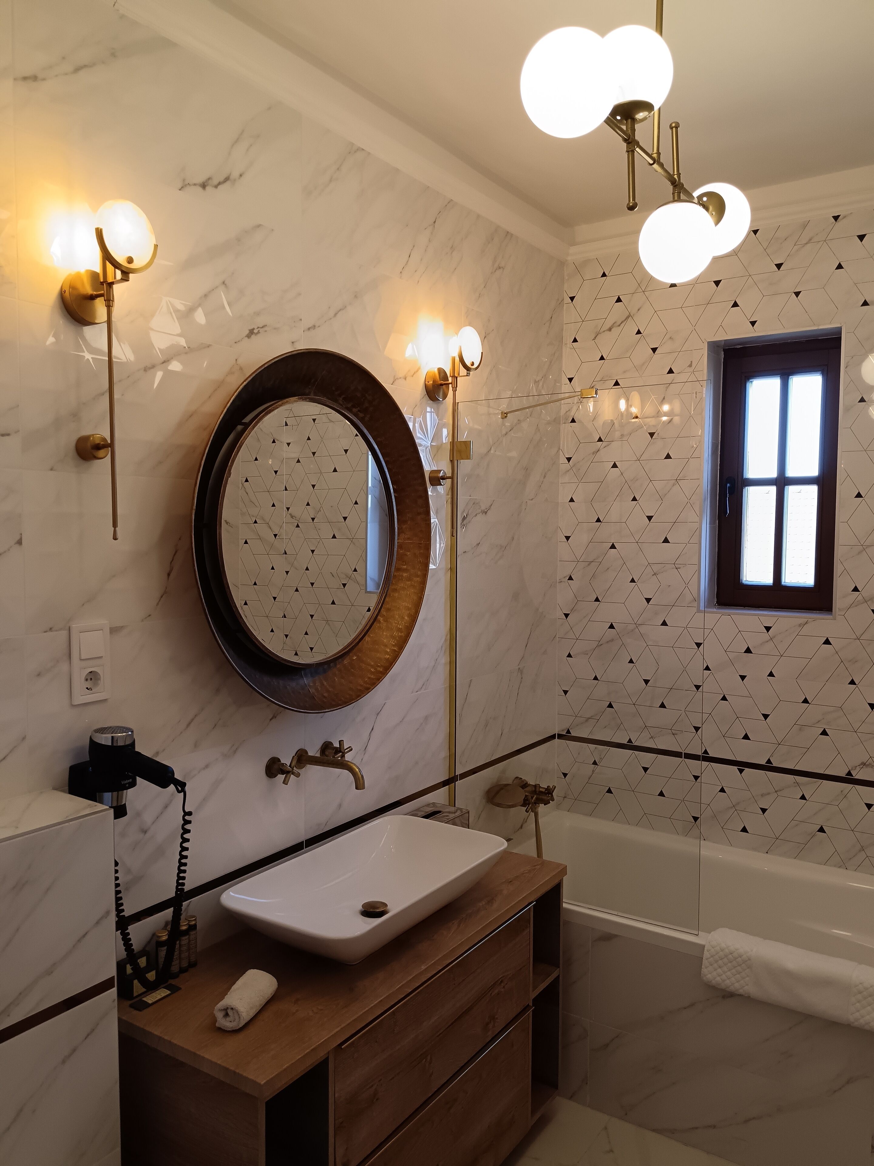 A bathroom with a round mirror, a sink, a bathtub, and a window.