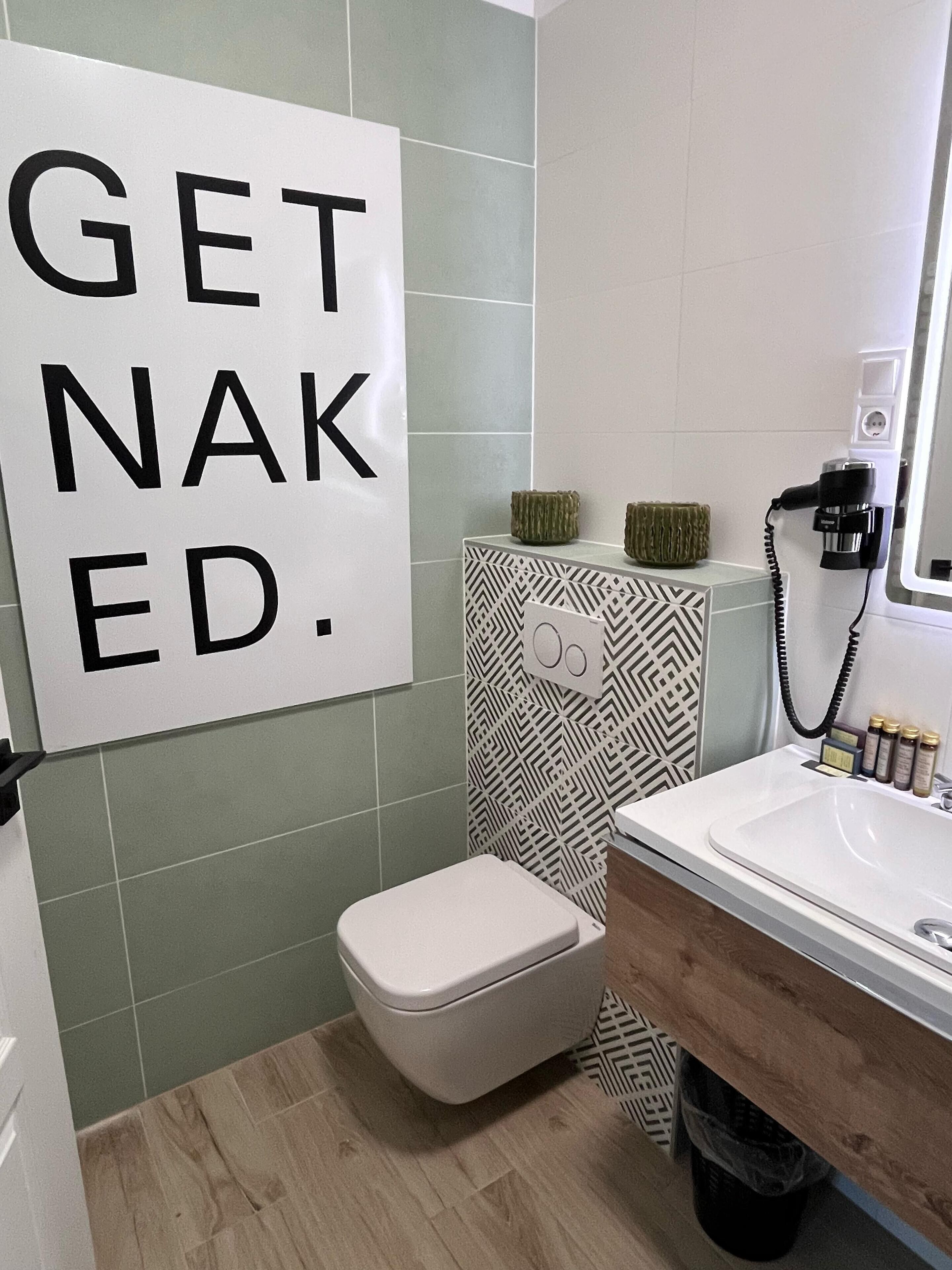 Un baño con inodoro, lavamanos y un cartel que dice 'GET NAKED'.