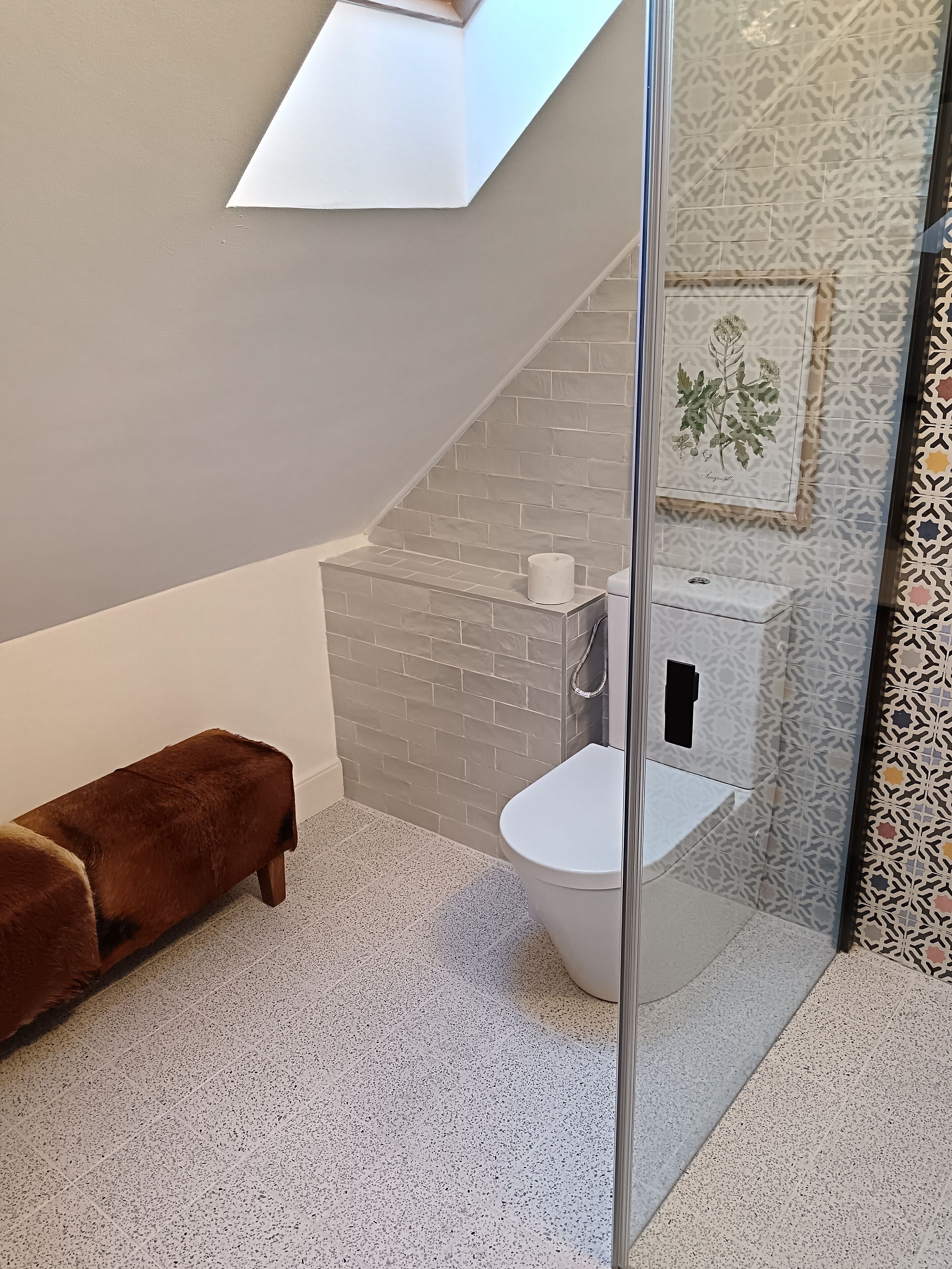 Un baño moderno con inodoro blanco, un banco marrón y un tragaluz.