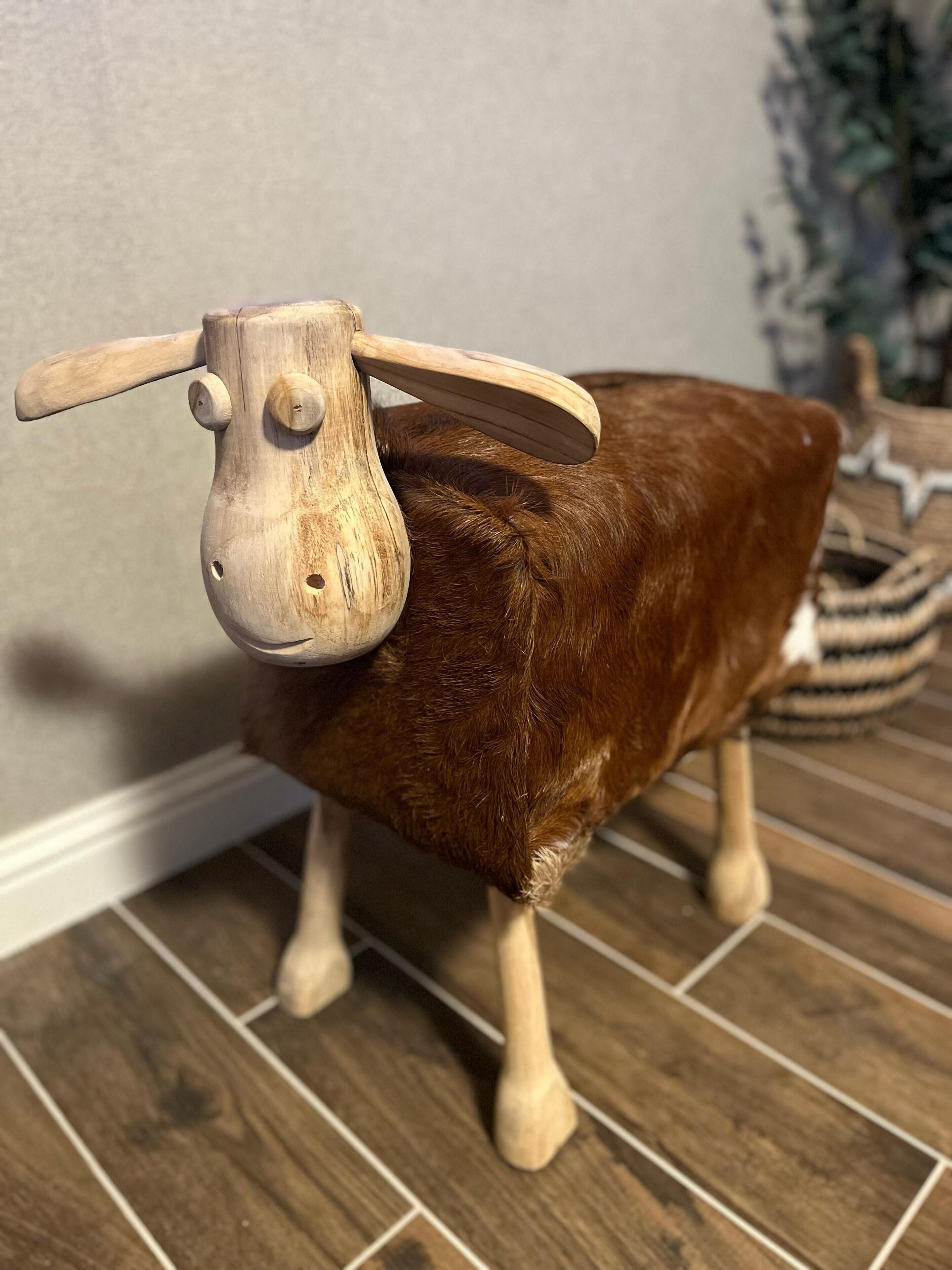 Une sculpture en bois représentant un mouton, avec un corps marron et une tête et des pattes en bois clair.