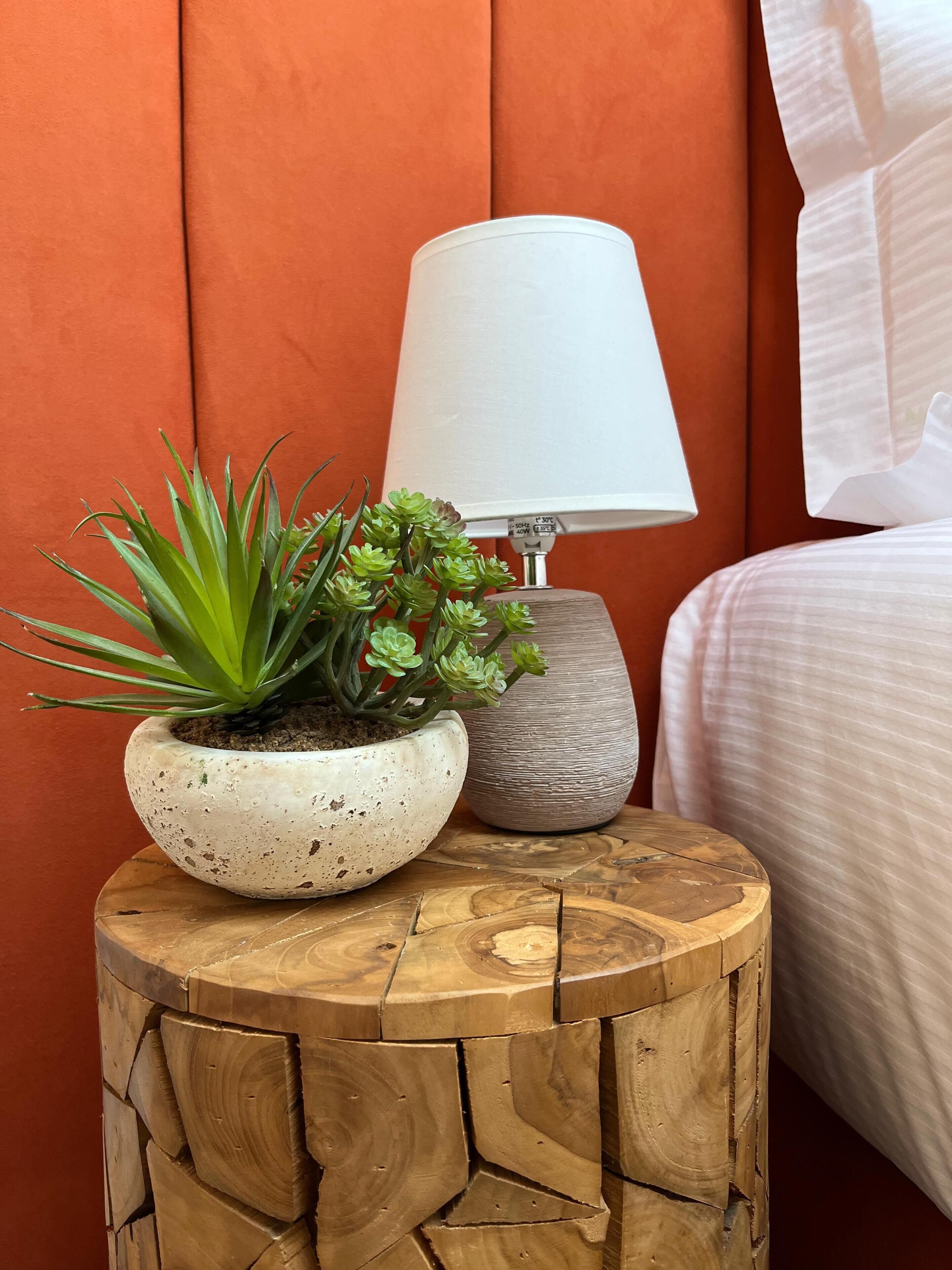 A wooden stool with a potted plant and a lamp against an orange wall.