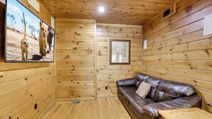 Interior de una cabaña de madera con un sofá de cuero, una mesita y un cuadro en la pared.