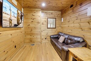 A wooden cabin interior with a leather sofa, a small table, and a framed picture on the wall.