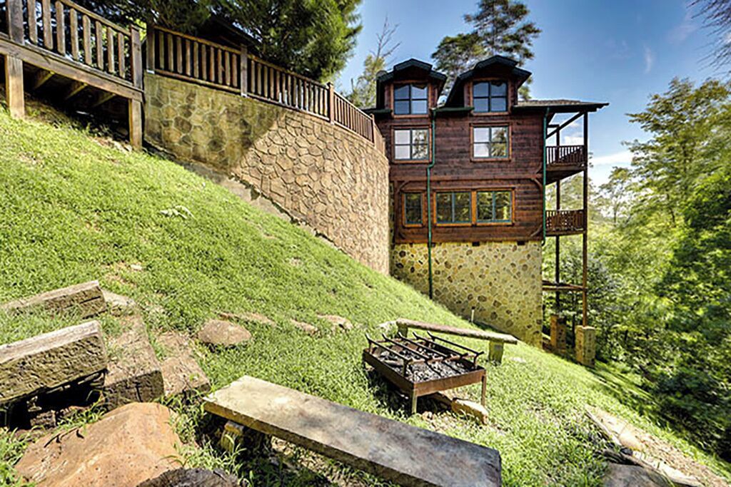 Une maison rustique en bois, dotée d’un mur de soutènement en pierre, d’une terrasse en bois et d’une cheminée en pierre.