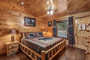 A wooden cabin bedroom with a bed, nightstands, a window with curtains, and a door.