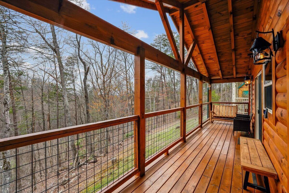 A wooden deck with a metal railing, a bench, and a view of a forest.