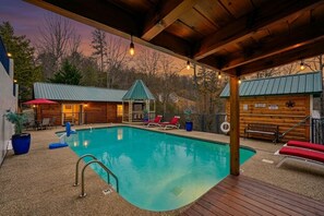 Une piscine avec des chaises longues, une terrasse couverte et un petit bâtiment doté d’un toit végétalisé.