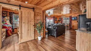 Interior de uma cabana de madeira com sala de estar, área de jantar e cozinha.