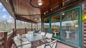 A wooden deck with a table and chairs, large windows, and a view of the outdoors. - Elegant Mountain Vista w/ Games & Hot Tub (Sevierville)
