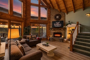 A spacious living room with a fireplace, wooden beams, and a large window overlooking a scenic view.