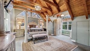 A spacious bedroom with a large bed, a bench, and a decorative rug. - Elegant Mountain Vista w/ Games & Hot Tub (Sevierville)