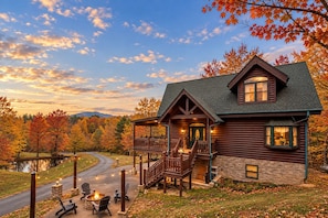 A log cabin with a porch, a fire pit, and a view of a lake.