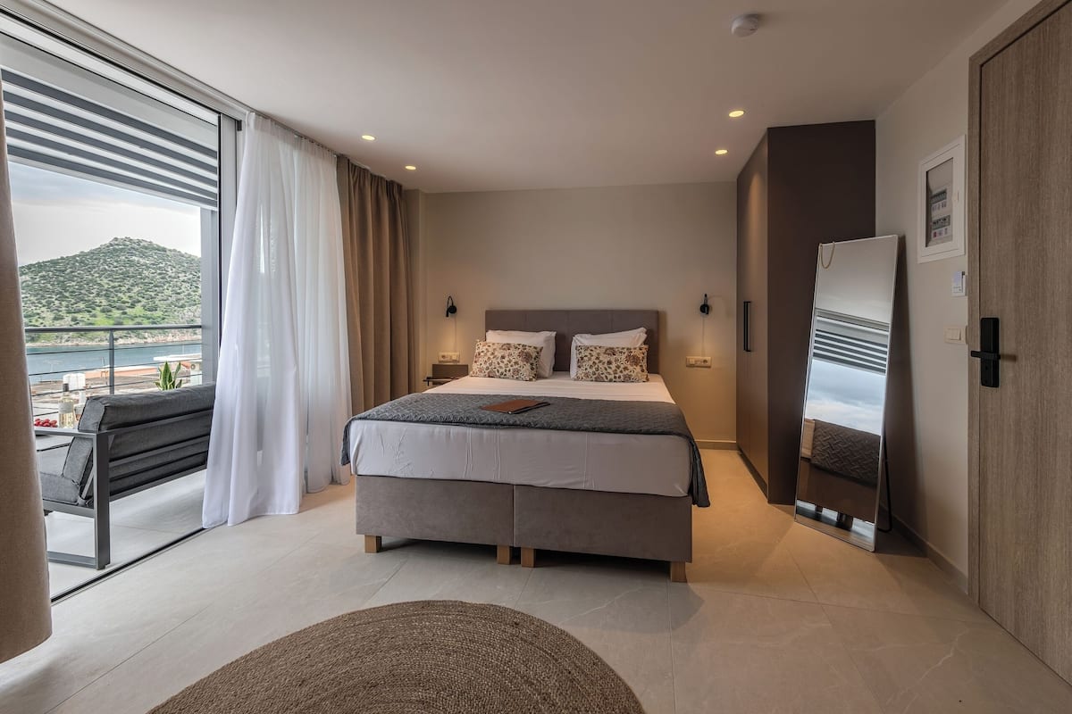 A modern bedroom with a large bed, a bedside table, a mirror, and a view of a balcony with a mountain in the background.