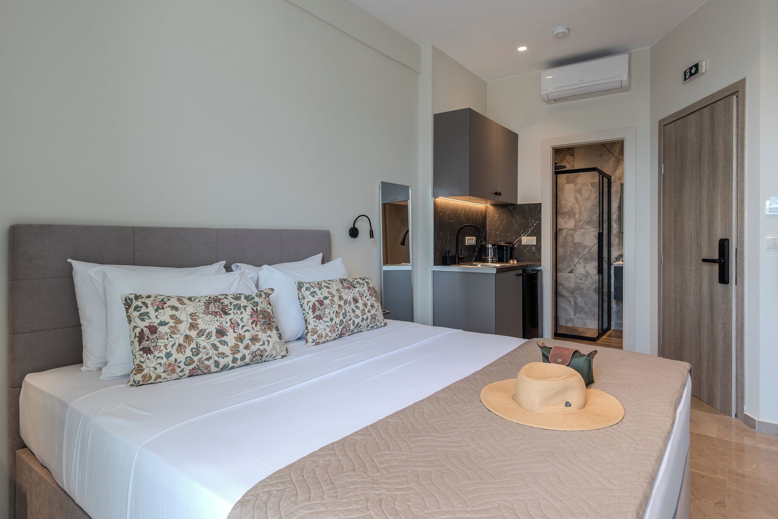A modern hotel room with a large bed, a kitchenette, and a bathroom visible through an open door.