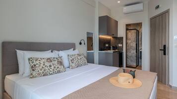 A modern hotel room with a large bed, a kitchenette, and a bathroom visible through an open door.