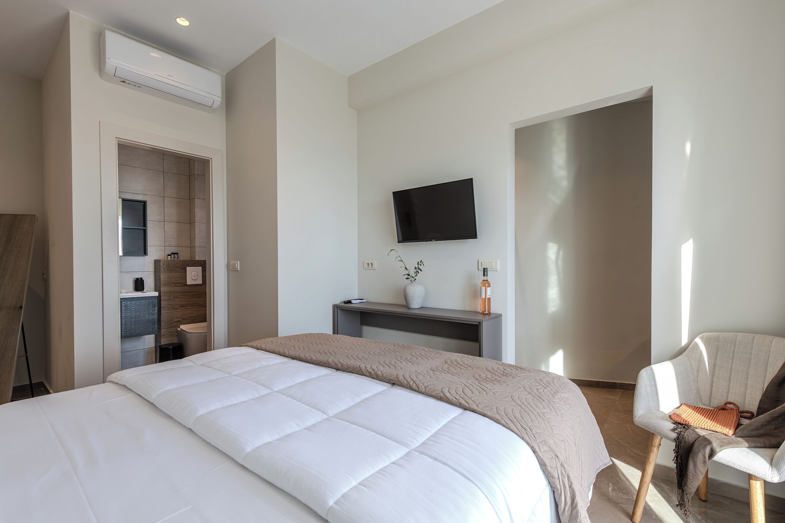 Ein modernes Hotelzimmer mit einem großen Bett, einem an der Wand montierten Fernseher, einer Sitzecke mit einem Sessel und einem kleinen Tisch.