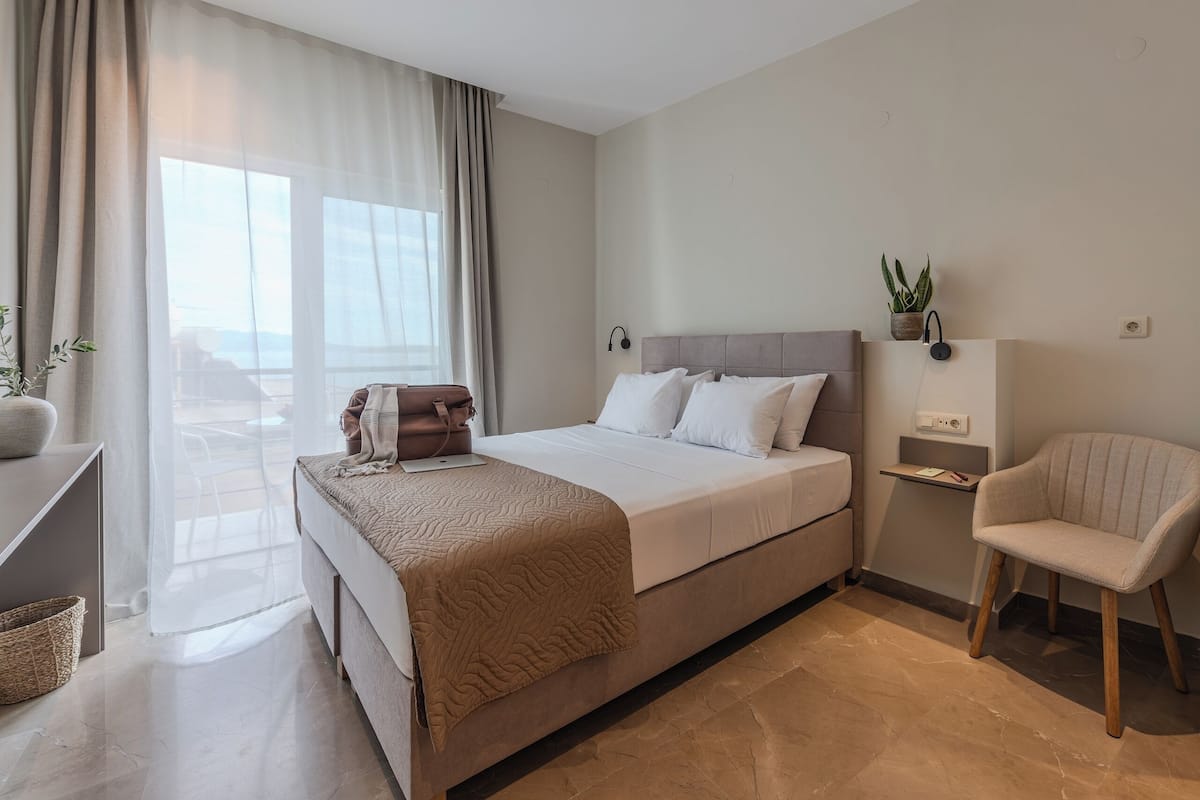 A modern hotel room with a large bed, a bedside table, a chair, and a view of the outdoors.
