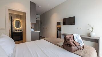 A hotel room with a bed, a desk, a TV, and a bathroom visible through an open door.