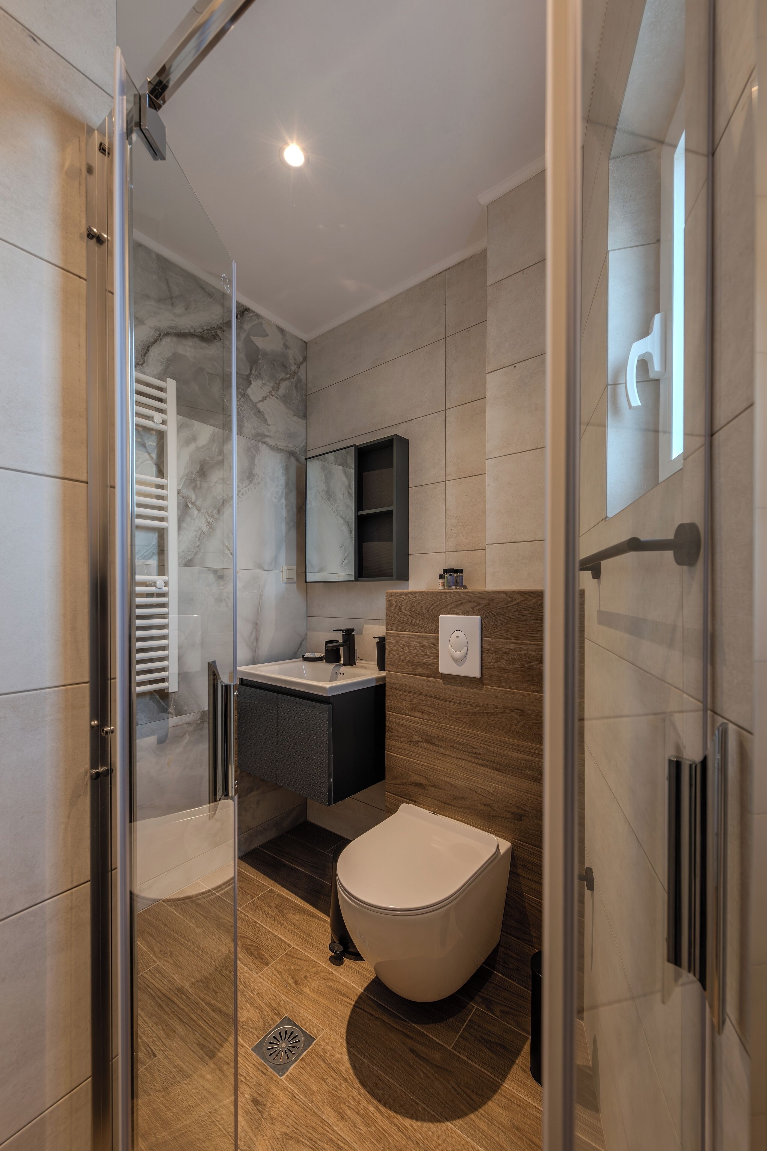 A modern bathroom with a glass shower enclosure, a wooden vanity, a marble backsplash, and a toilet.