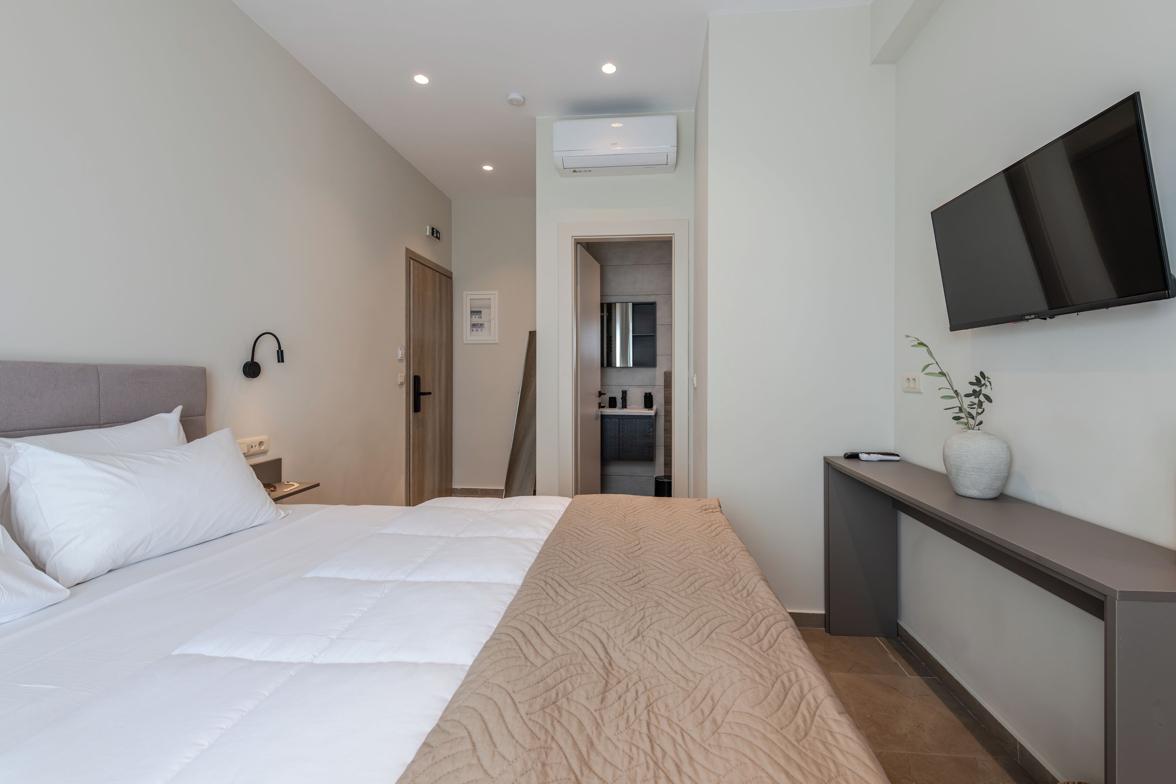 A modern hotel room with a large bed, a flat-screen TV mounted on the wall, a bedside table, and a small console table with a vase.