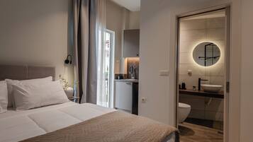 Une chambre d’hôtel moderne avec un grand lit, une petite kitchenette et une salle de bain dotée d’un miroir rond.