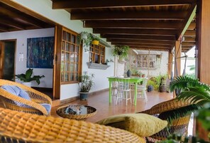 A covered outdoor seating area with wicker furniture, a table, and potted plants.