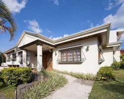 A two-story house with a front porch, a window with metal bars, and a small garden area with plants and a stone pathway.