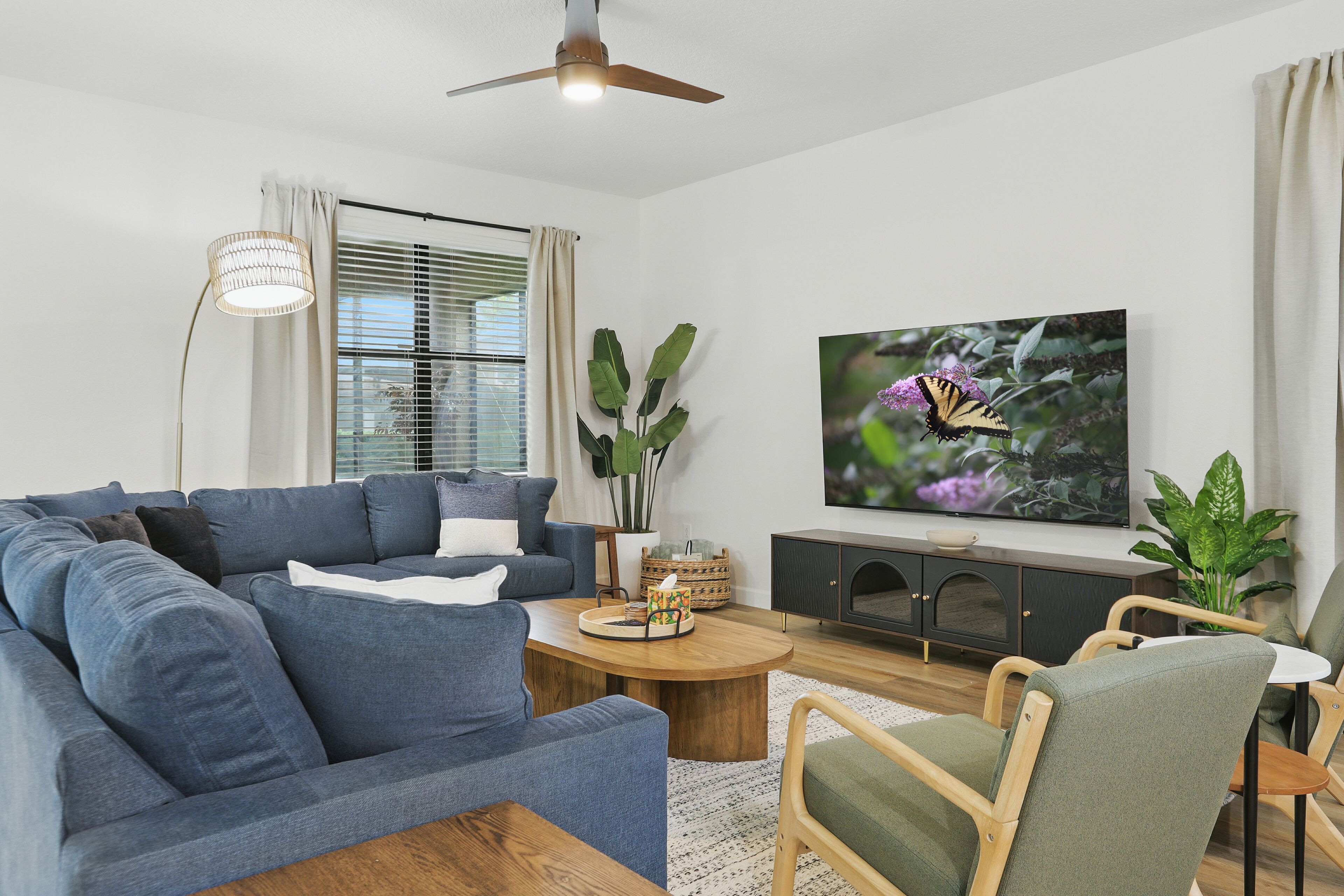 A modern living room with a blue sofa, a wooden coffee table, a TV on the wall, and a ceiling fan.